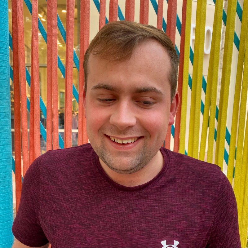 Ethan stands in front of a colorful background, smiling at the camera.